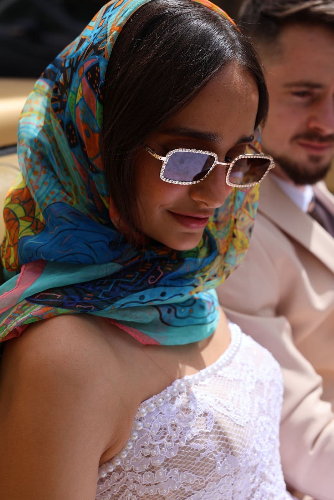 A bride in a vivid silk headscarf and jewelled sunglasses beside her partner