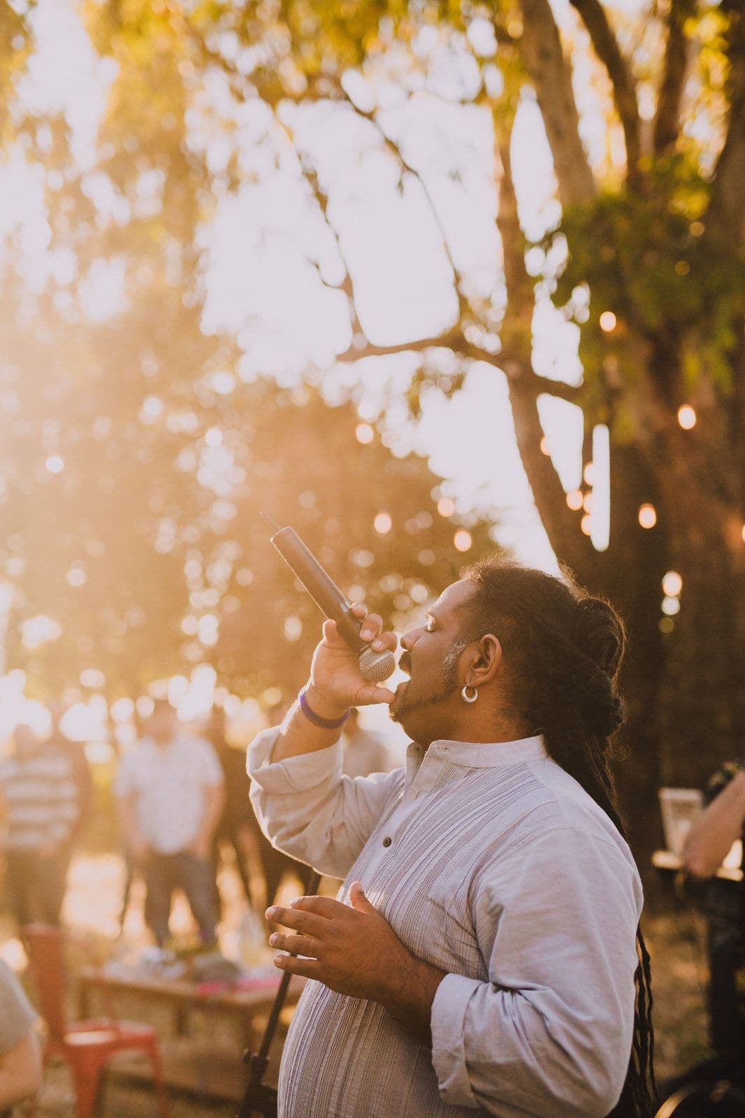A singer with a microphone performing under the trees in golden light