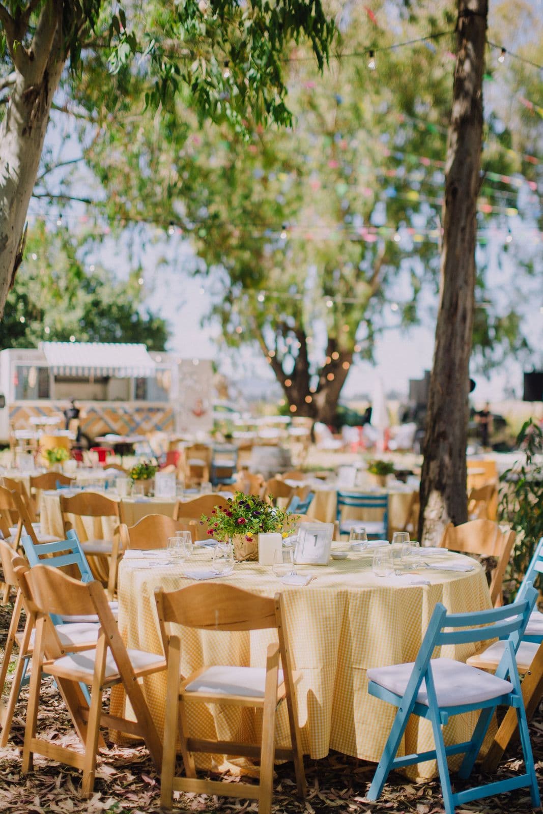 Wooden tables and blue chairs set for a wedding under the trees